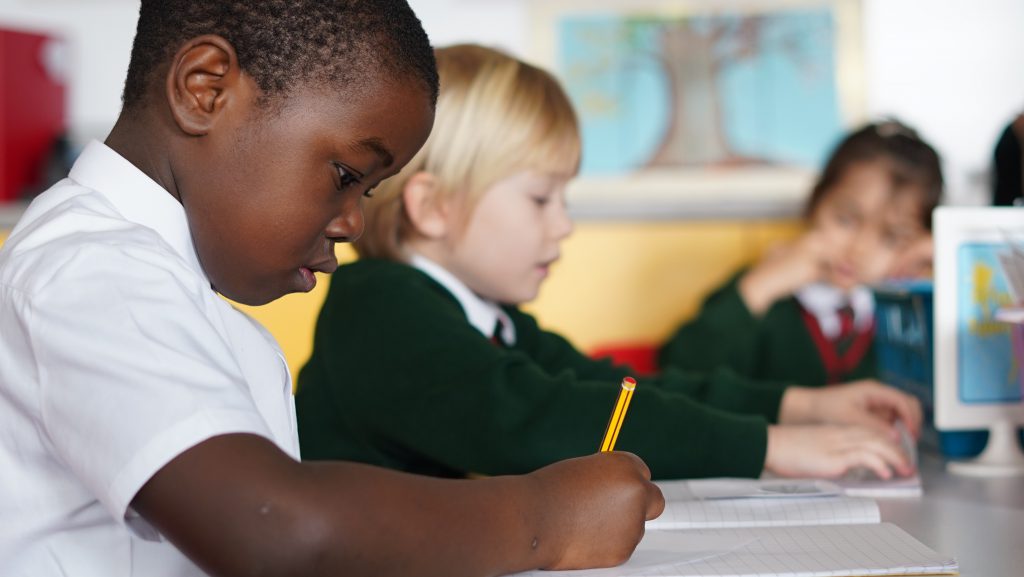 A young boy and girl writing in a classroom.