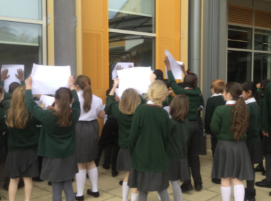 A large group of students holding up banners against a window on the academy building.